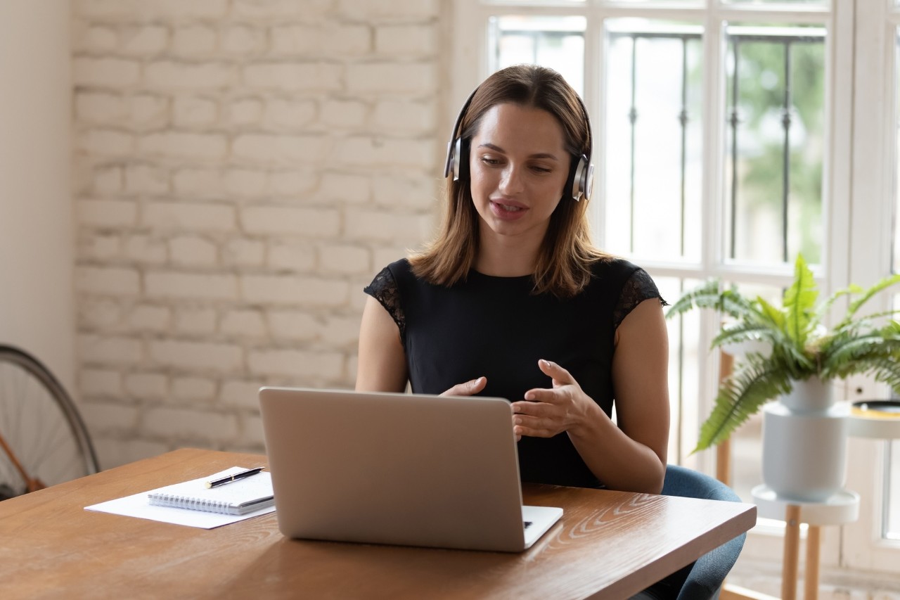 Zelfverzekerde jonge zakenvrouw die een draadloze hoofdtelefoon draagt en projectdetails bespreekt met klanten via een videogesprek. Intelligente, ervaren vrouwelijke werknemer-spreker die een online ontmoeting met collega's houdt.