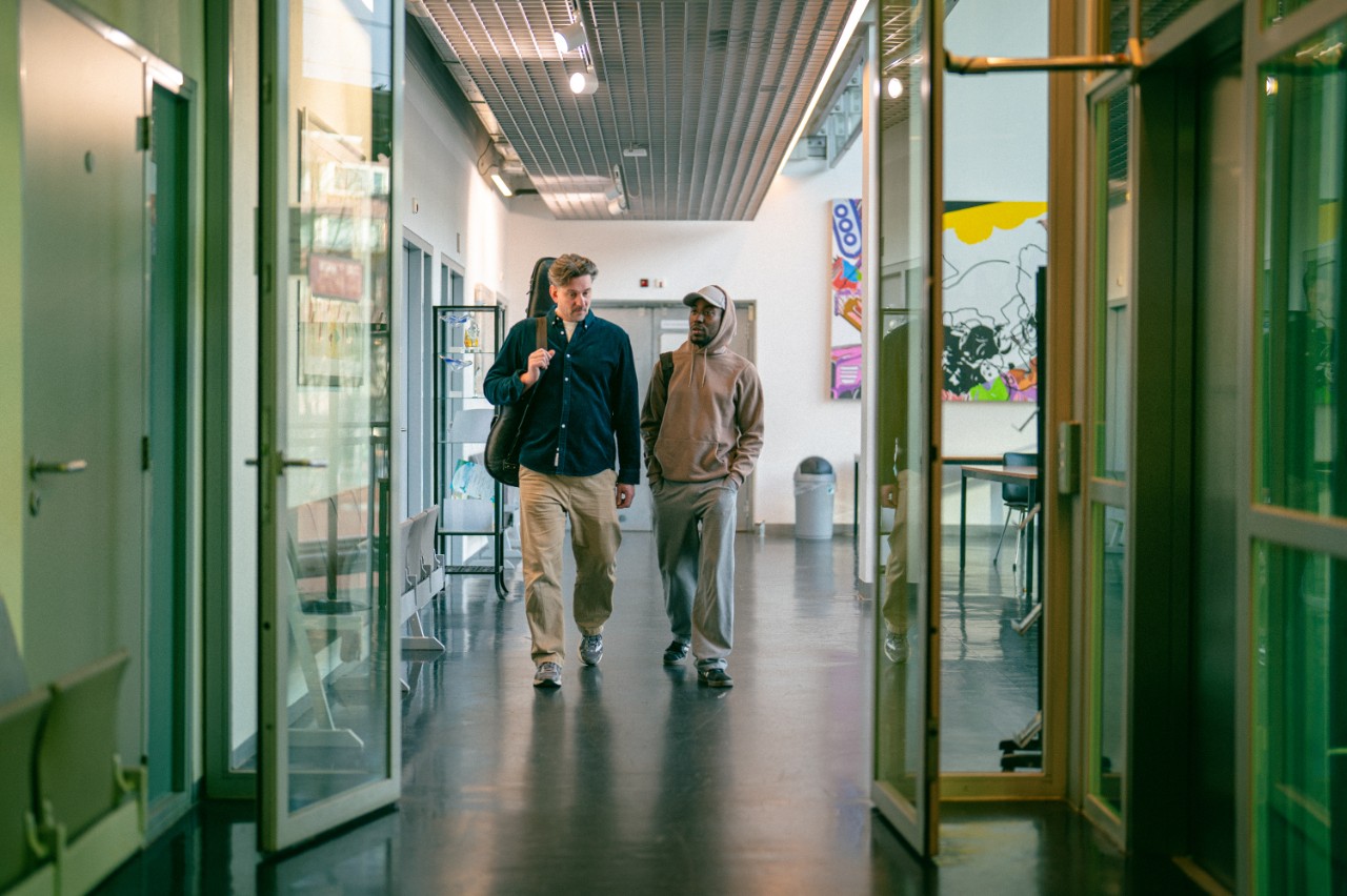 Twee mannen lopen met instrument door gang van een creatieve school