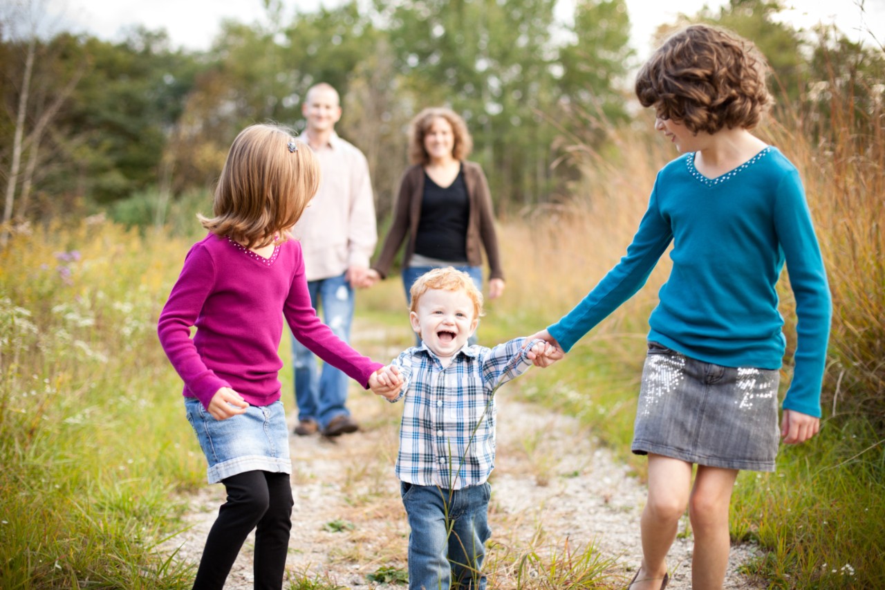 Color image of a happy family of five with dad, mom, two little girls, and a toddler son, walking together outside on a fall day.
