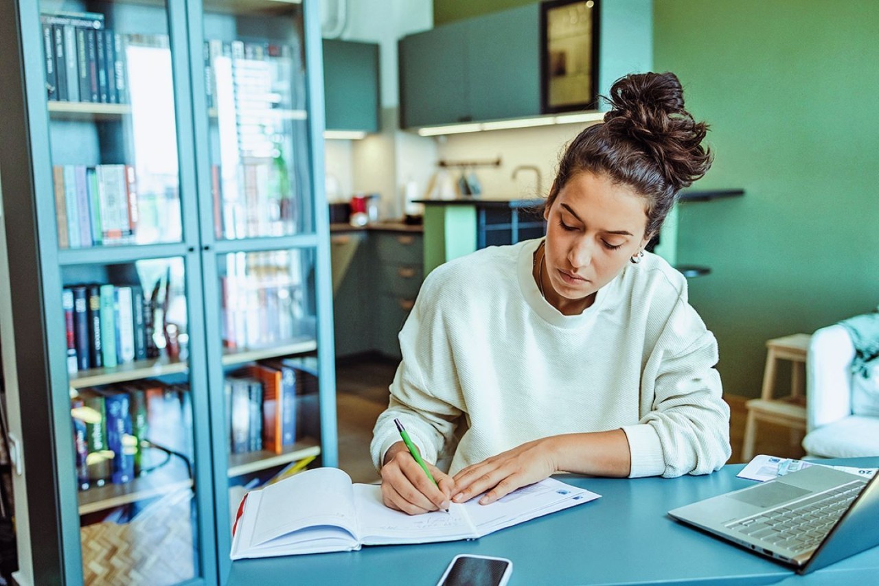 Vrouw zit achter laptop en schrijft op papier