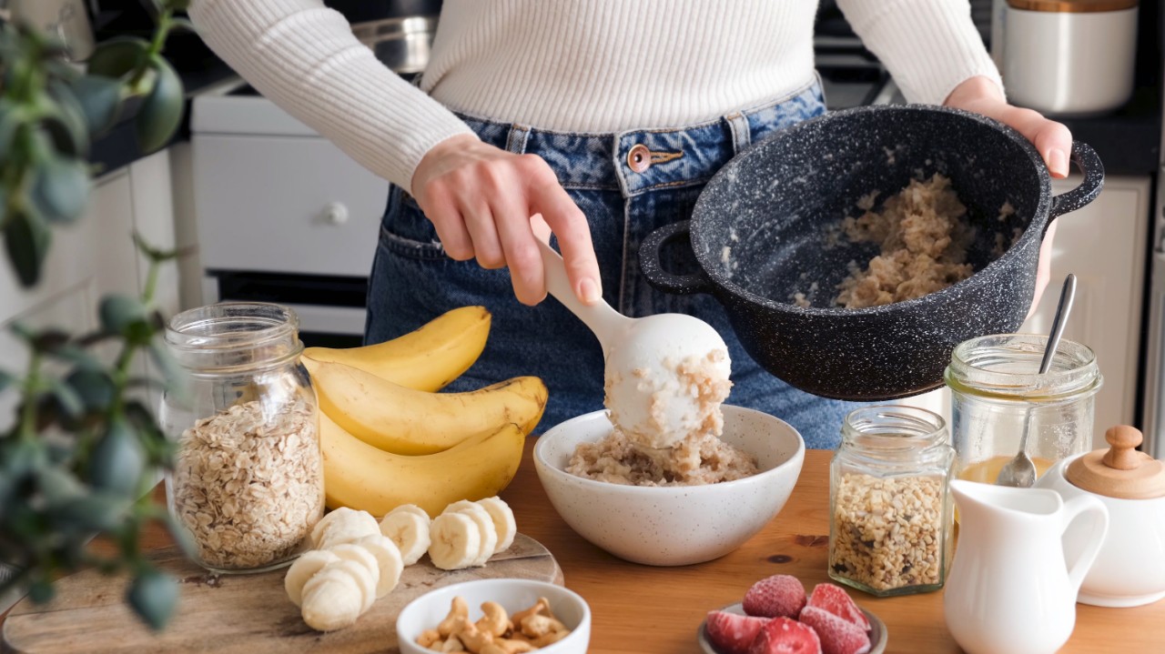 Woman putting oatmeal in a bowl with spoon. Preparing healthy breakfast at the kitchen. Healthy lifestyle concept