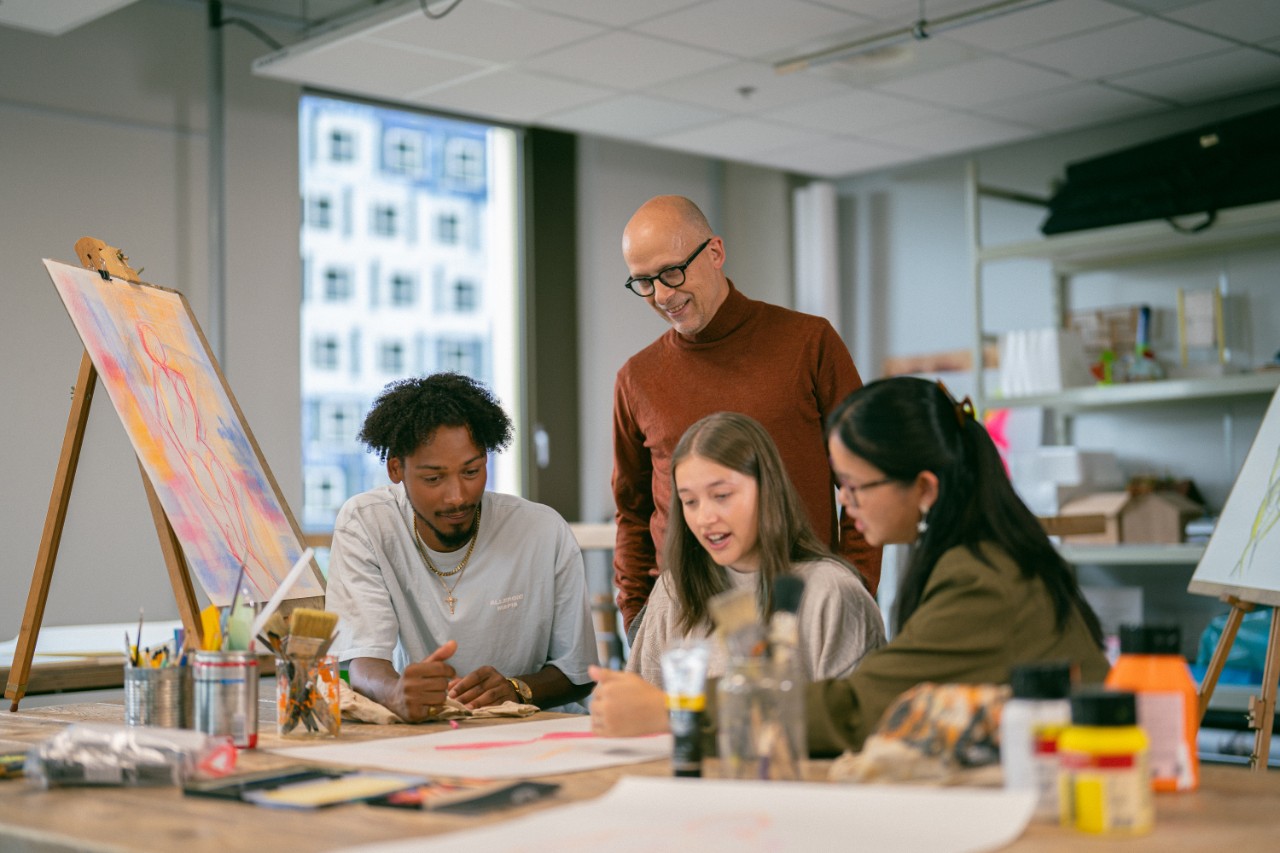 Docent kijkt mee met 3 leerlingen kunst