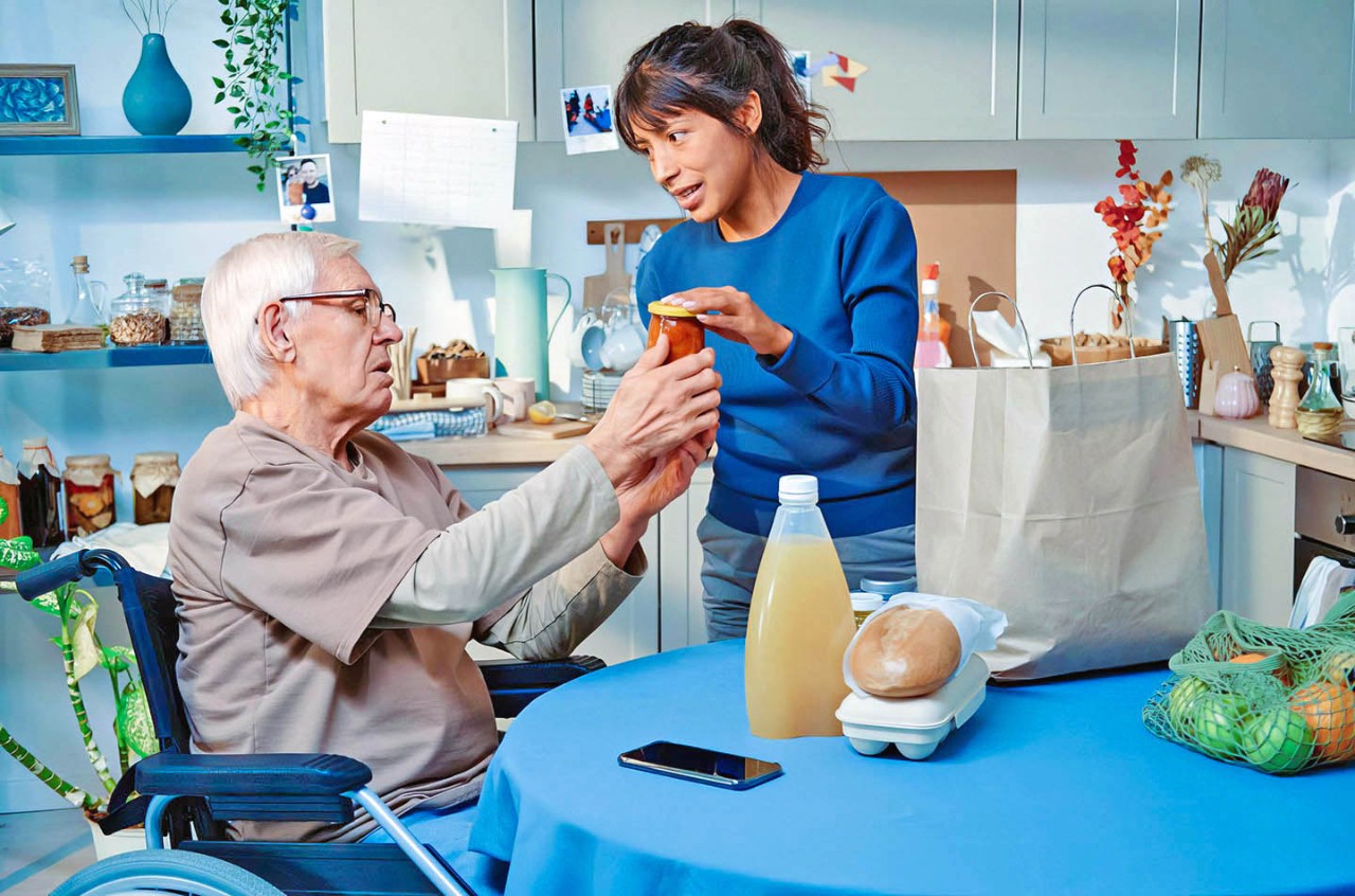 Verzorgster geeft pot uit boodschappentas aan man in rolstoel