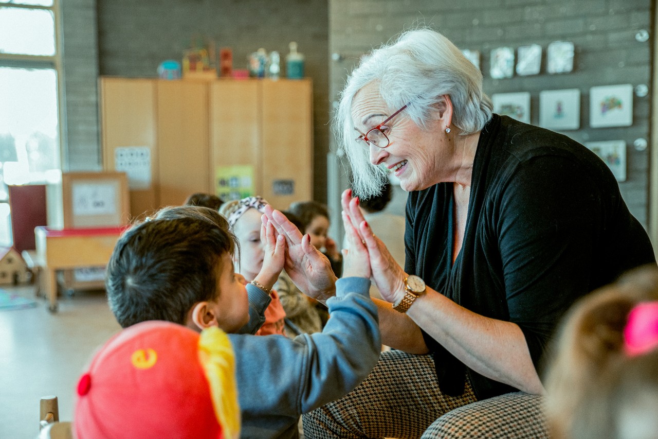 Oudere kinderjuf geeft high five aan peuter