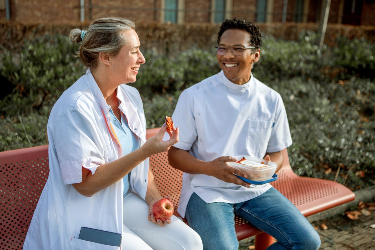 HR-twee verpleegkundigen met lunch buiten op bankje