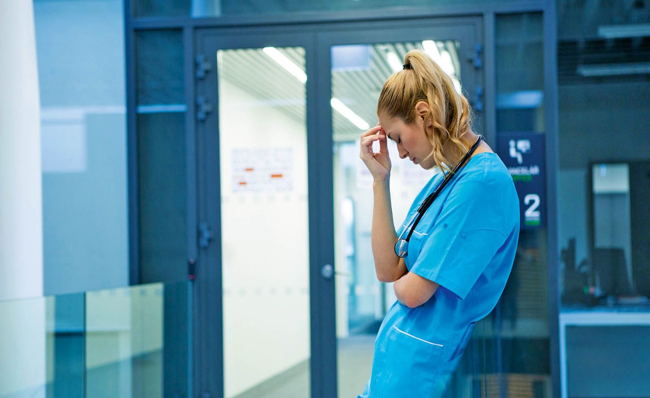 verpleegkundige staat op werkvloer gefrustreerd met hand tegen het hoofd
