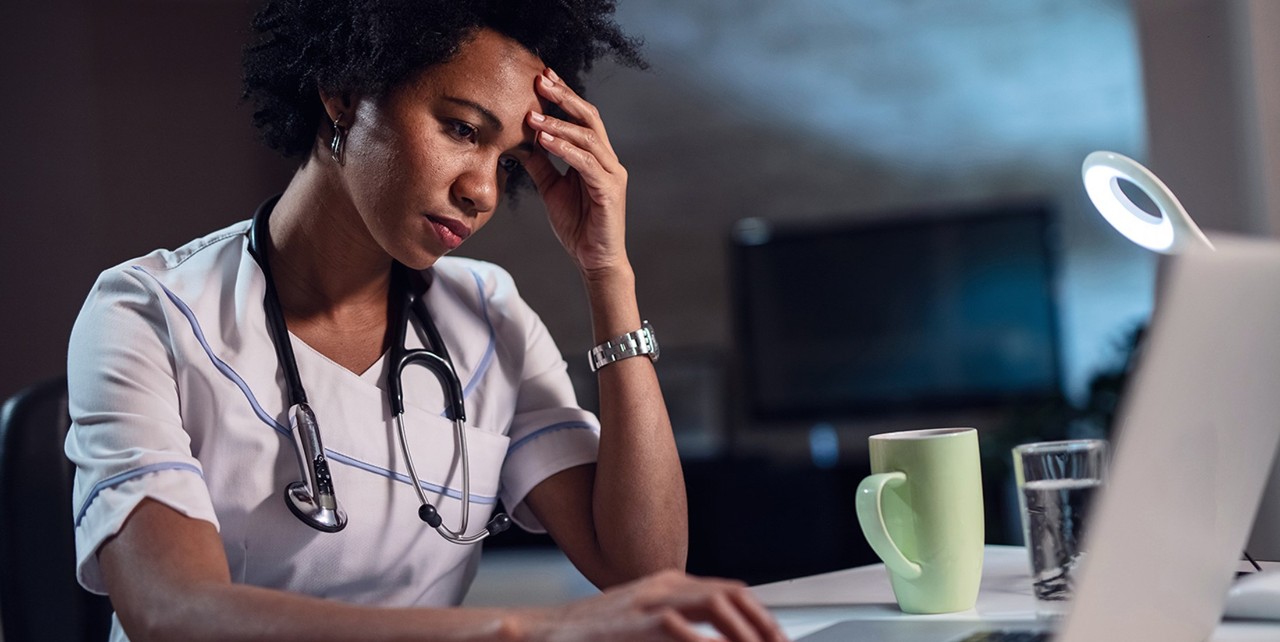 Displeased black healthcare worker using computer and reading an e-mail at doctor's office.