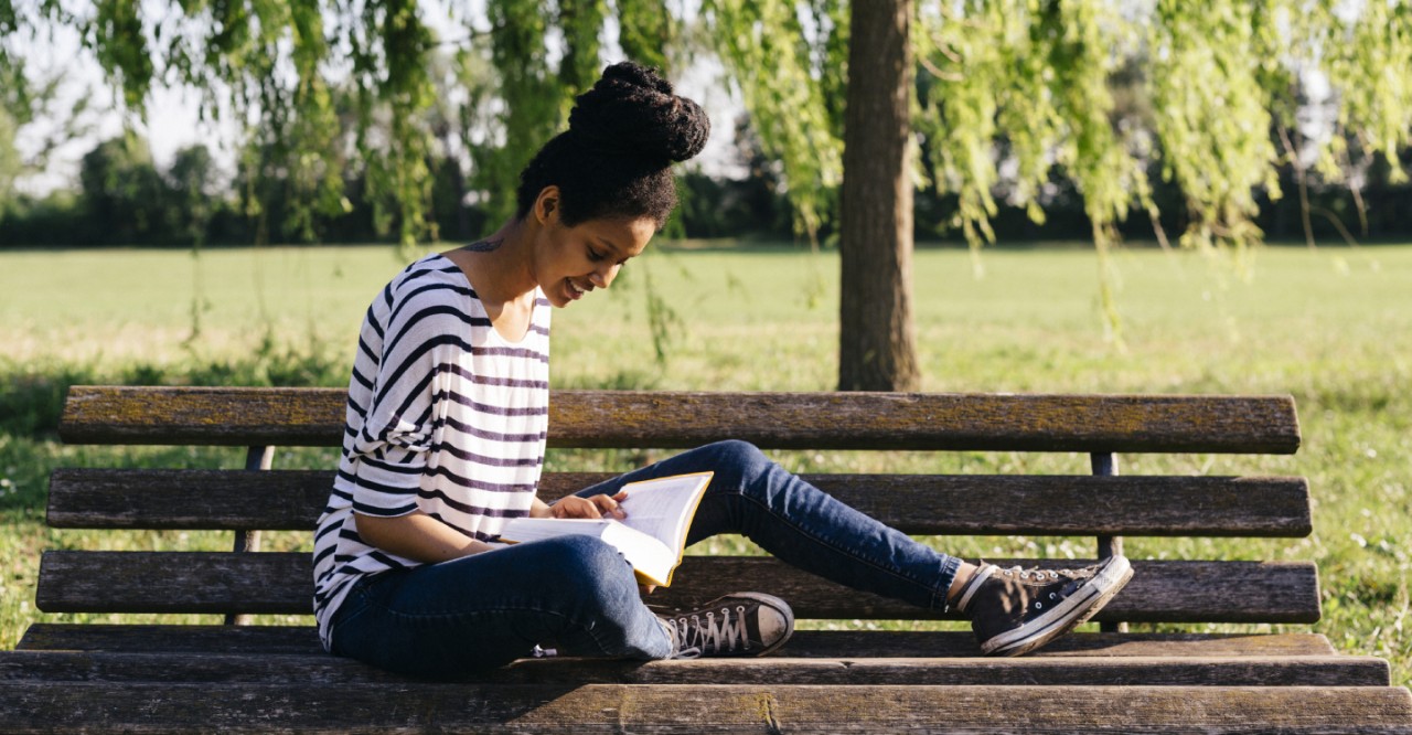 Vrouw leest boek op bankje buiten