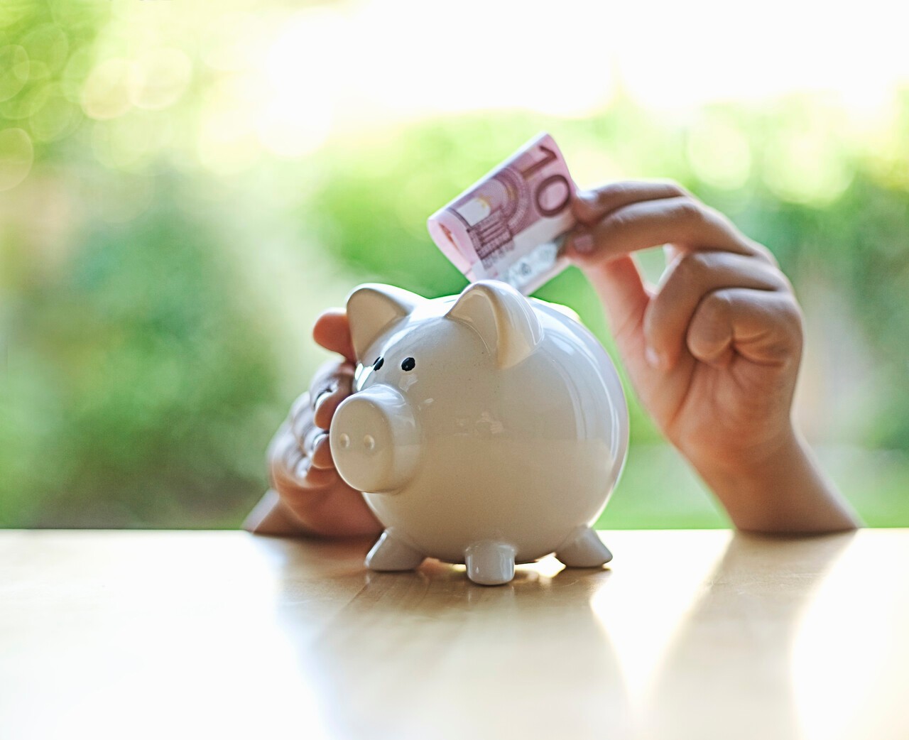 Twee handen stoppen 10 euro in spaarvarken