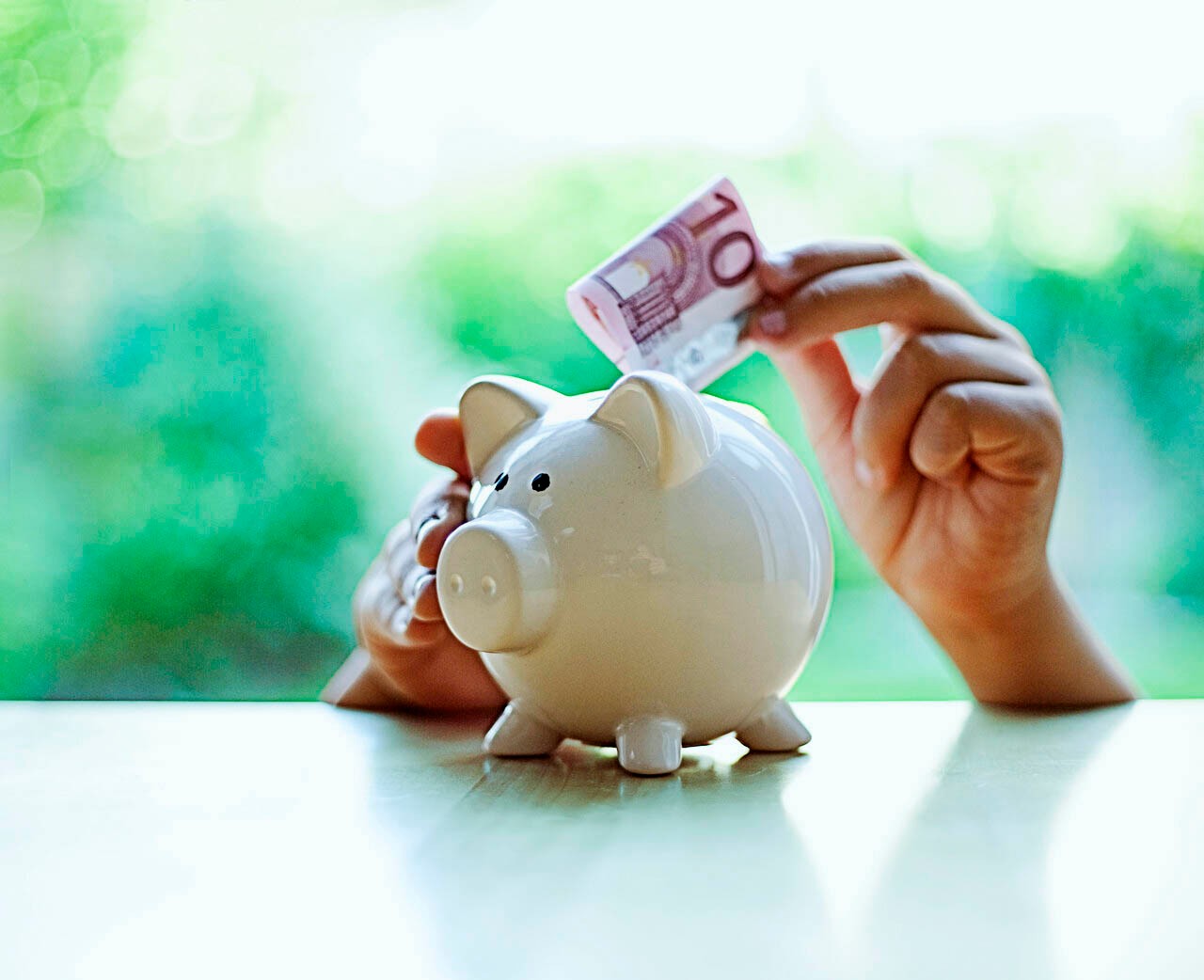 Twee handen stoppen 10 euro in spaarvarken