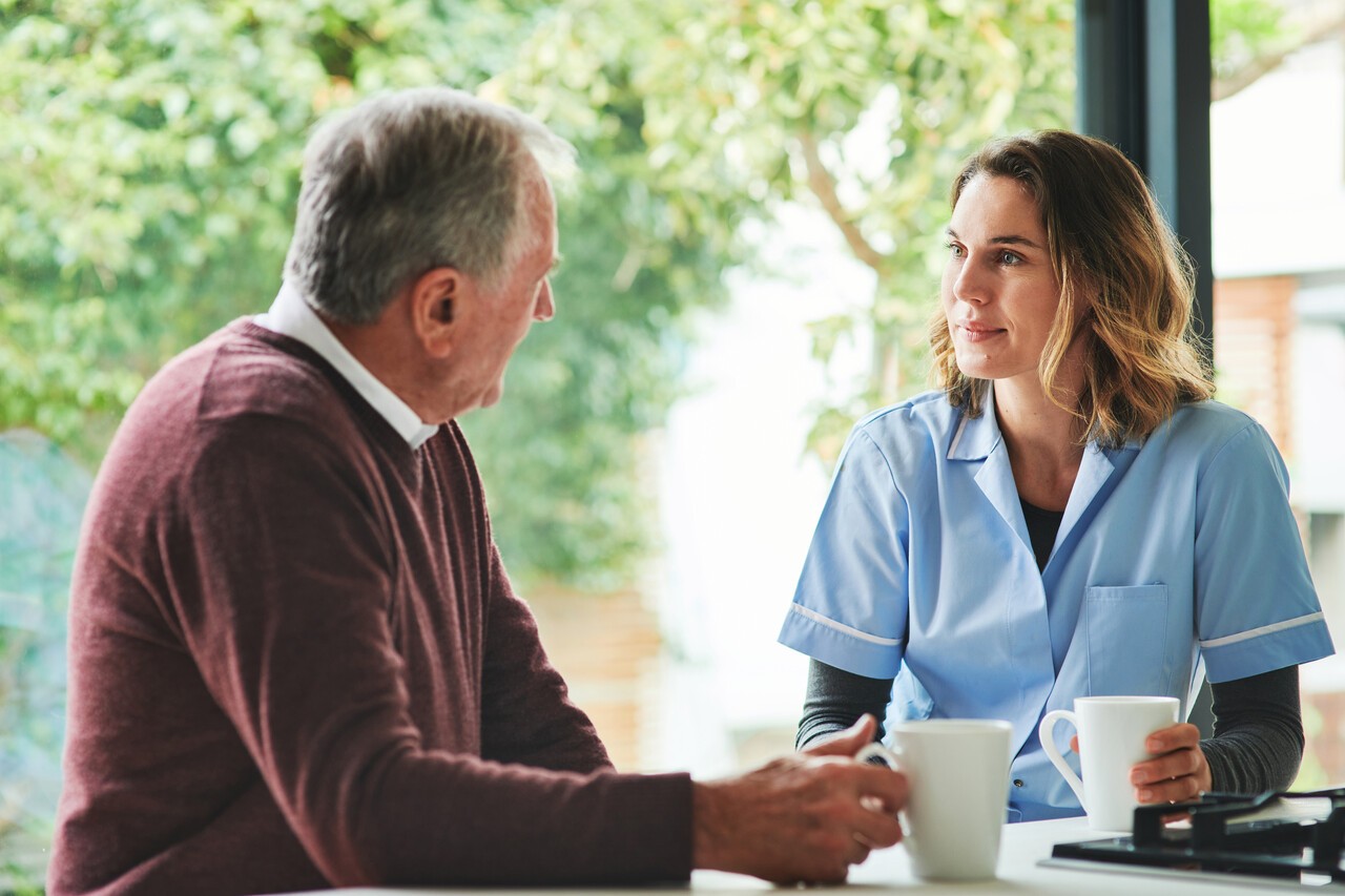 Zorgmedewerker en man drinken koffie aan tafel