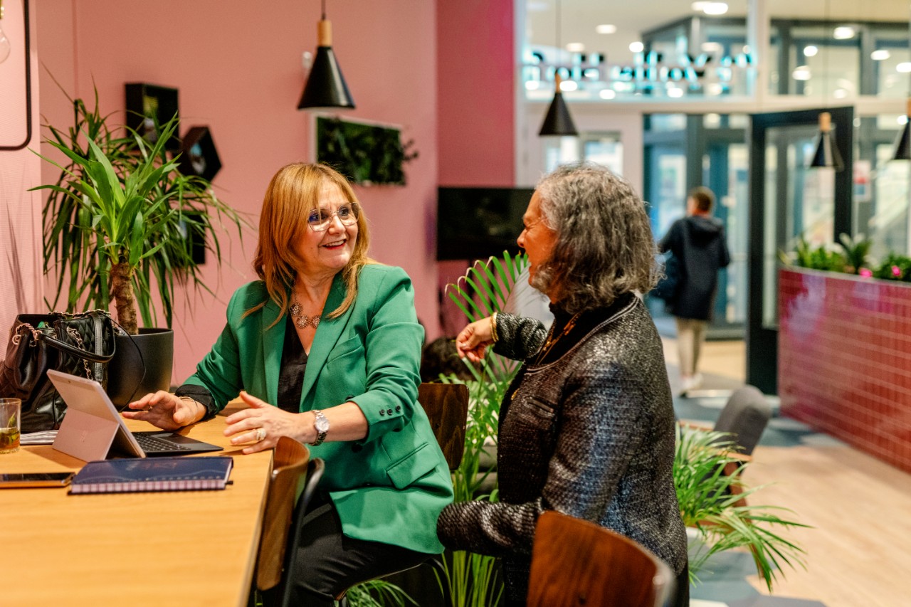 Twee vrouwen in gesprek bij ipad in kleurrijke omgeving