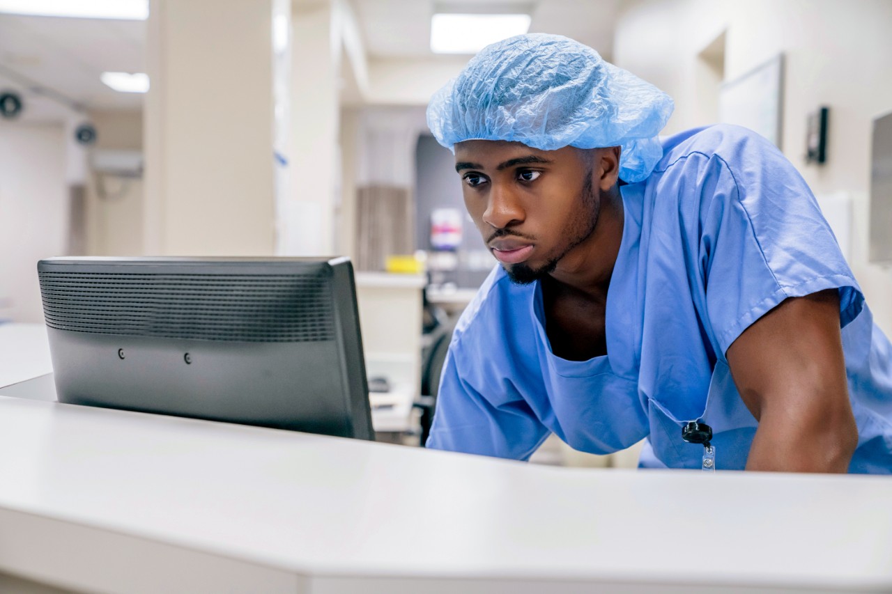 Verpleegkundige met blauw haarnetje achter PC bij de balie