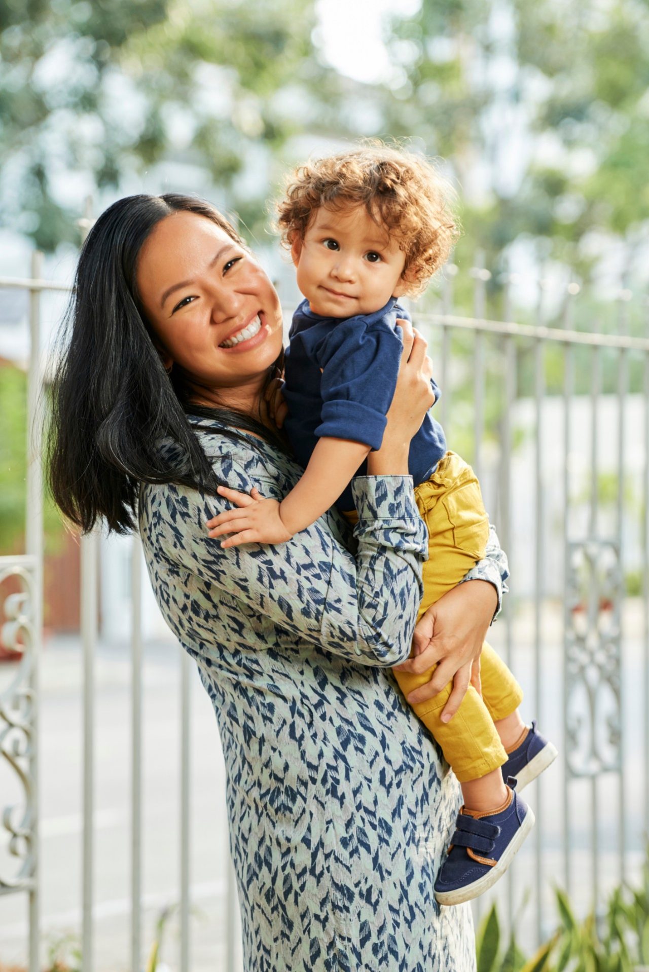 Portrait of smiling mother holding little son in hands when standing in backyard of house